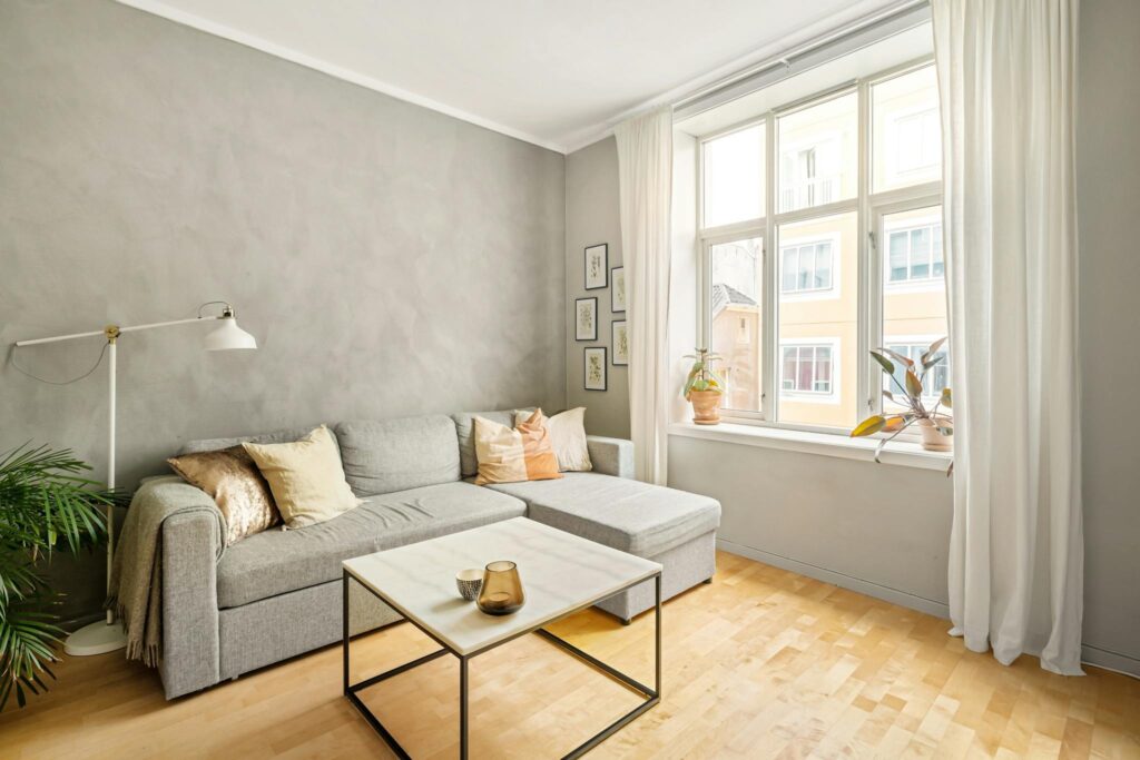 A bright and cozy modern living room featuring a gray sofa and large window for natural light.